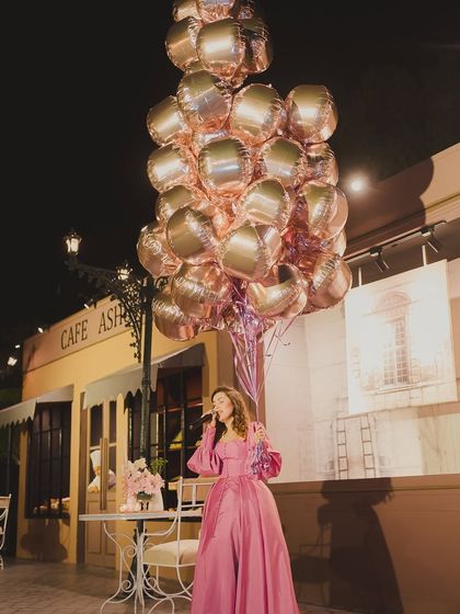 A performer in a stunning pink gown, holding a large bouquet of balloons, creates a whimsical and picture-perfect moment on the cafe-style stage.