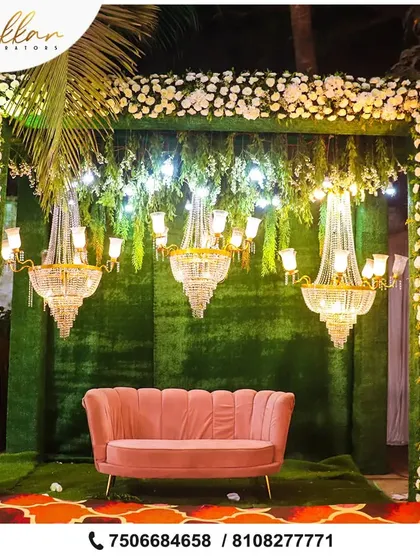 A beautiful and elegant photo booth or seating area. The green backdrop is adorned with white flowers and chandeliers, creating a sophisticated and intimate space.