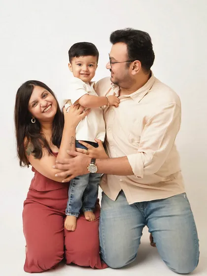 A joyful and candid family photo capturing a mother and father kneeling and embracing their toddler, who is standing between them with a huge smile. This shot shows the fun and energy of a family photoshoot with an older child.