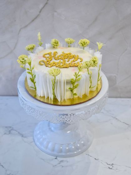 A chic and delicious chocolate hazelnut cake. The design is simple yet elegant, with delicate white chocolate floral details and a gold "Happy Birthday" topper.