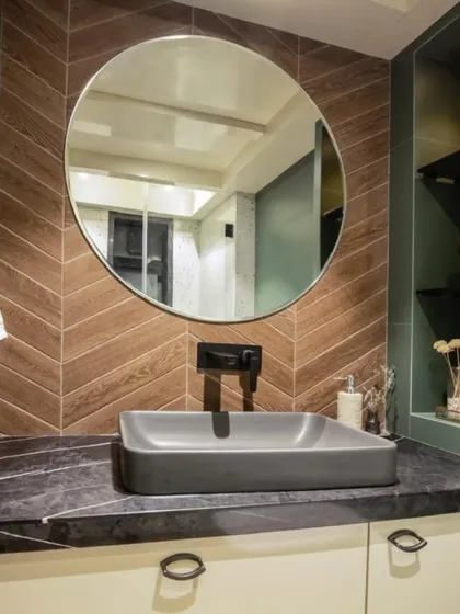 A beautiful example of a functional and aesthetic washroom. The combination of green walls, wood-textured tiles in a herringbone pattern, and a simple round mirror creates a fresh and modern look.