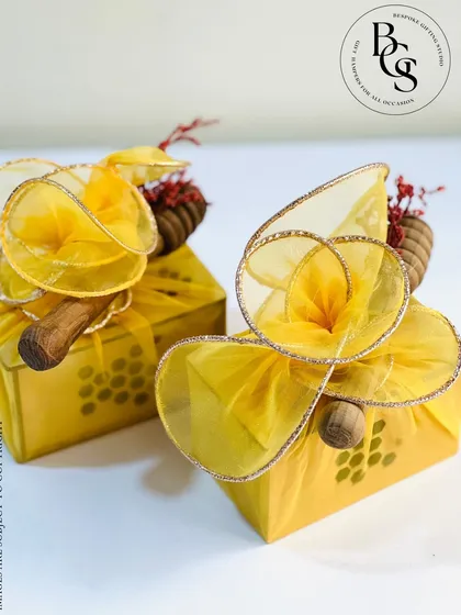 A unique take on gift wrapping, these yellow patterned boxes are adorned with a sculptural organza bow and a rustic wooden handle detail. This creative presentation is sure to make your gift stand out.