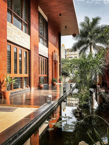 A tranquil water body runs alongside the exposed brick exterior of this contemporary villa in Hennur. This feature is central to our design philosophy of integrating natural elements like water and greenery into the living space.