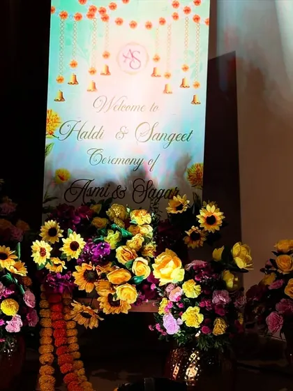 A personalized welcome sign for a joint Haldi and Sangeet ceremony, surrounded by beautiful arrangements of sunflowers and other colorful blooms.