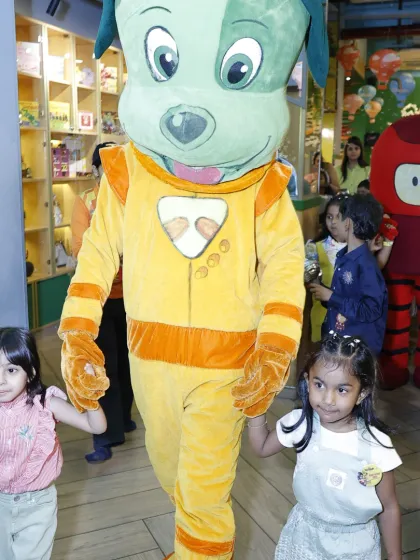Tinga Dojo and Popsy lead a parade through the play area, with two little girls happily holding Tinga's hands.