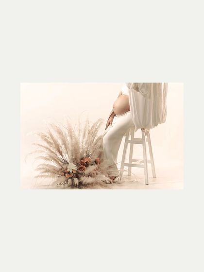 A minimalist studio setup with pampas grass. This cropped shot focuses on the texture of the dried florals and the mother-to-be's hand on her belly, creating an artistic and serene composition.