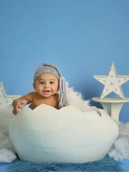 A half-birthday celebration with a celestial theme. This 6-month-old is sitting in a cracked egg prop, surrounded by a moon, stars, and clouds.