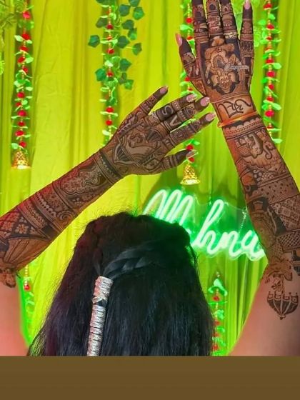 A fun shot of a bride showing off her mehendi from behind, with a "Mehndi" neon sign in the background.