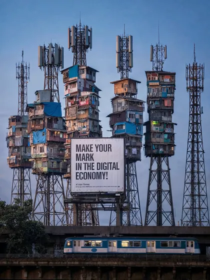 A view of 'Network Nagar' with a train passing by and a large billboard that reads 'MAKE YOUR MARK IN THE DIGITAL ECONOMY!'. This adds a layer of corporate propaganda and social commentary to the scene.