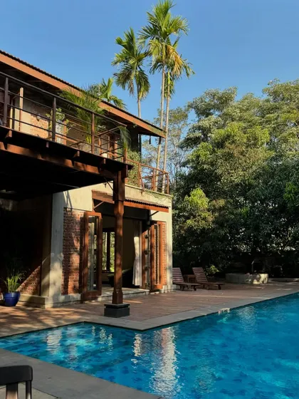 The poolside at The Mango House. The architecture, with its blend of brick, wood, and concrete, sits comfortably amidst the palm trees and lush greenery of Awas village in Alibag.