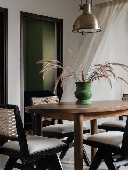 This dining area is the yin to the living room's yang. The simple wooden table with black and cane chairs creates a minimalist, chic look. A vintage green enamel vase adds a pop of color, subtly connecting to the green wardrobe visible in the adjacent room.