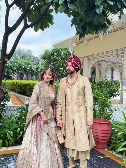 A full view of the coordinated couple's outfits. The bride's flowing lehenga and the groom's structured sherwani create a beautiful balance, showcasing how individual styles can merge into one harmonious story.