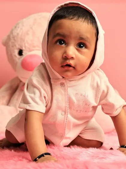 This curious baby was photographed in a simple studio setup with a pink backdrop and a teddy bear. See the next image for the transformation.