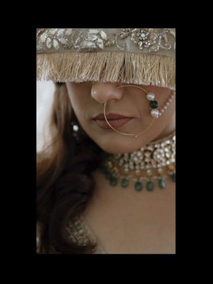 A close-up, artistic shot of a bride's face, her nose ring and jewelry in focus, her face partially obscured by her veil.