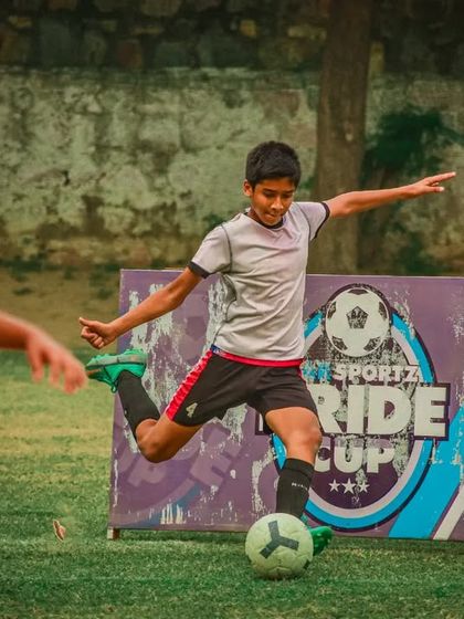 A player shoots at goal in front of the Sar Sportz Pride Cup banner.