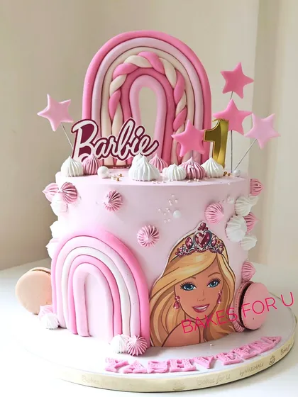 A dreamy two-tier Barbie cake for a first birthday, decorated in shades of pink with fondant rainbows, stars, and an edible image of Barbie. This design is perfect for a little one's special milestone.