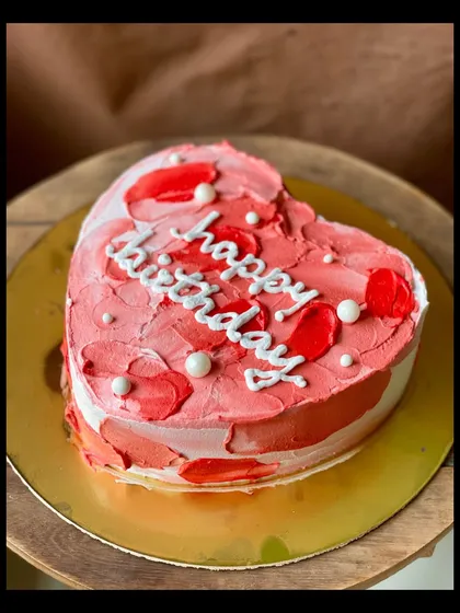 A heart-shaped birthday cake with textured red and pink buttercream. The pearl sprinkles add a touch of elegance.