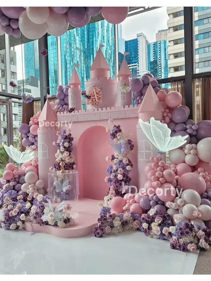 A fairytale comes to life with this stunning pink princess castle backdrop. Surrounded by a sea of pink and purple balloons and glowing butterflies, it's the perfect stage for a royal celebration.