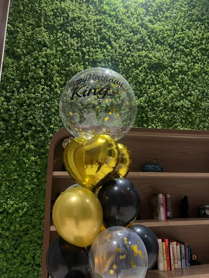 A close-up of our 'Happy Birthday King' helium balloon bouquet. The gold confetti inside the bubble balloon adds a touch of sparkle to the black and gold theme.