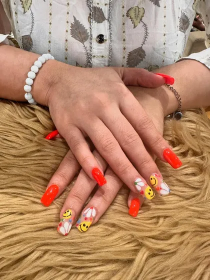 A full view of the long, square-shaped nails with bright red and playful smiley face art, showing off a fun and confident style.