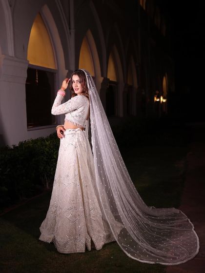 A dramatic night shot of a bride in a white chikankari lehenga with a long, flowing veil. This is a look that is both modern and timeless.