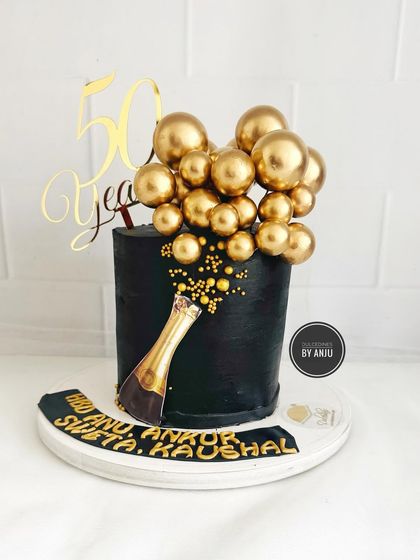 A glamorous 50th anniversary cake. This black cake with a champagne bottle popping golden bubbles is perfect for a grand celebration.