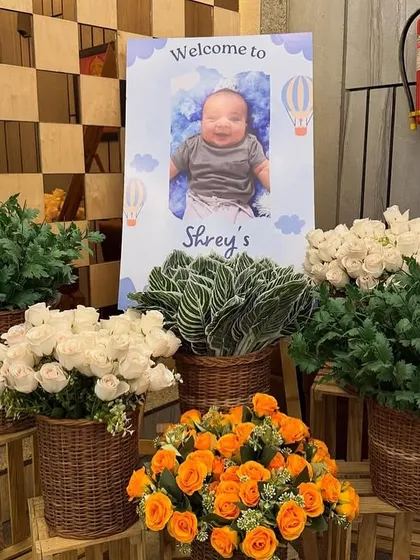 A personalized welcome sign for baby Shrey's party, surrounded by beautiful fresh flower arrangements in baskets.