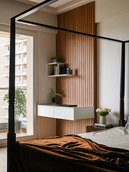 This bedroom features a classic four-poster bed, which adds a touch of timeless elegance. Adjacent to it, a floating white console table is set against a wooden fluted wall, creating a functional and stylish study nook.