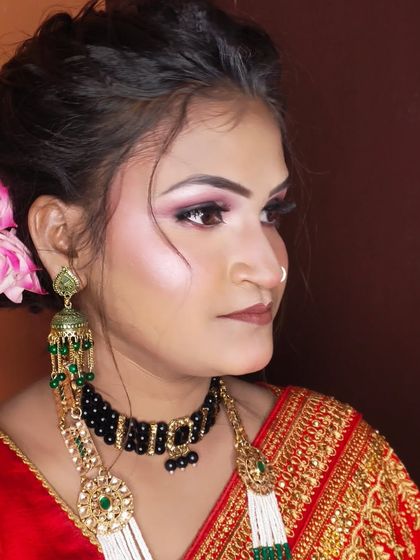 A side profile of a client ready for a party in a traditional red saree. The makeup is glamorous with smokey eyes.