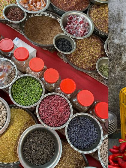 A collage of spices and produce, with vibrant red chillies next to bowls of colorful lentils and beans.