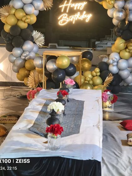 A view from the seating area towards the black, silver, and gold balloon backdrop, complete with a neon sign, perfect for a birthday dinner.