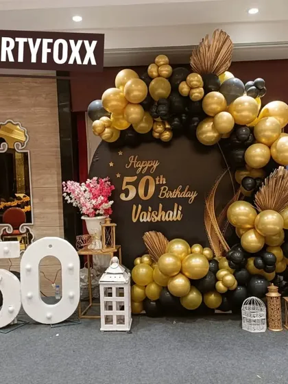 A sophisticated black and gold theme for Vaishali's 50th birthday party. This elegant setup includes large marquee numbers, a custom circular backdrop, and beautiful floral accents.