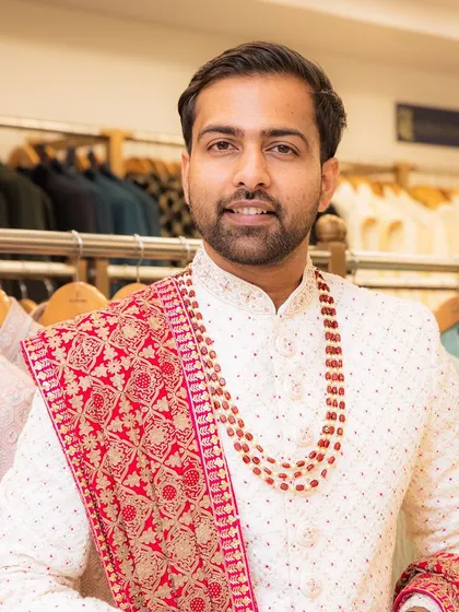 This client looks ready for his wedding day in our classic white sherwani, perfectly complemented by a red beaded mala and a matching embroidered red stole.