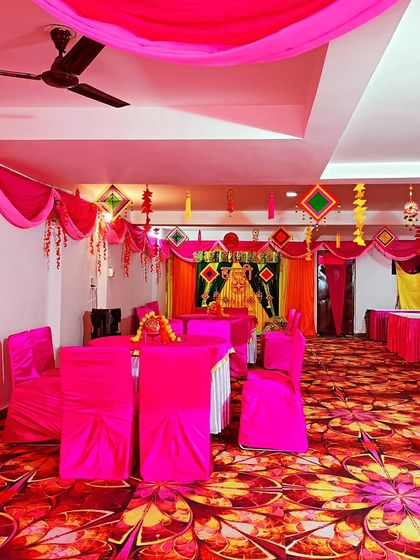 An indoor Haldi ceremony setup with the entire hall decorated in a vibrant pink theme, including chair covers, table cloths, and ceiling drapes.