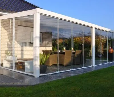 A prefabricated sunroom attached to a home, seamlessly extending the living space into the garden. This white-framed glass structure is furnished as a dining area, demonstrating a practical and popular use for our custom garden rooms.