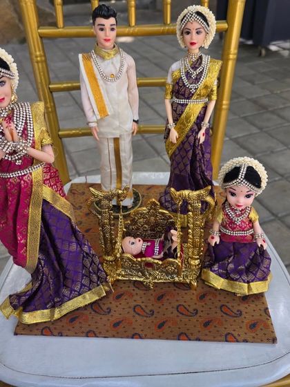 A charming detail from a naming ceremony, featuring custom dolls representing the family around a miniature golden cradle.
