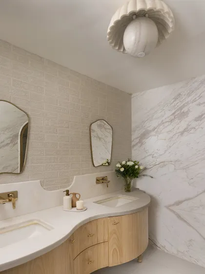This master en-suite at Ecru Maison features a custom curved vanity in light oak, topped with a shaped counter. The mix of marble, textured wallpaper, and brass fixtures creates a soft, luxurious feel.