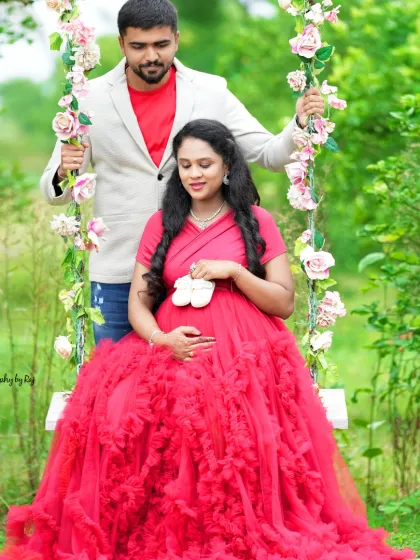 A sweet couple's portrait on our floral swing, holding tiny baby shoes. The mother-to-be is wearing a vibrant red ruffled gown.