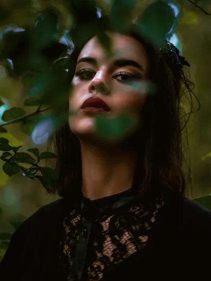 A close-up portrait from the jungle editorial. Peeking through the leaves adds a sense of mystery and intimacy, drawing the viewer into the frame.