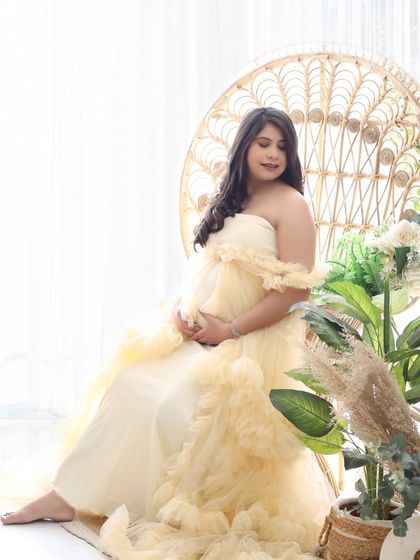 A soft and dreamy portrait in a pastel yellow ruffled gown. The mom-to-be is seated on a peacock chair, creating a gentle and romantic boho look.