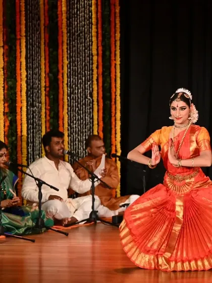 Kavya Navani in a moment of devotion during her arangetram, with the live orchestra providing the soulful musical foundation. This image captures the synergy between the dancer, the musicians, and the art form.