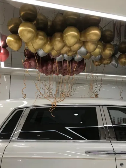 This image showcases the density of our helium balloon ceiling installations. Here, a mix of gold, silver, and burgundy balloons with flowing ribbons creates a rich, textured look over the vehicles in the showroom.