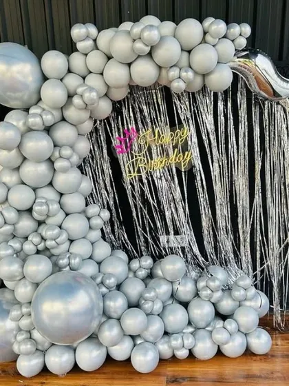 A modern birthday backdrop with a silver shimmer curtain and a full arch of silver balloons.