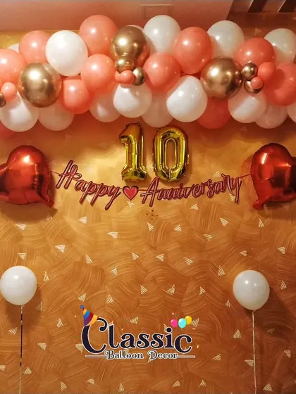 A simple wall decoration for a 10th anniversary. We created a balloon garland in peach and white, with a 'Happy Anniversary' banner and foil number and heart balloons.