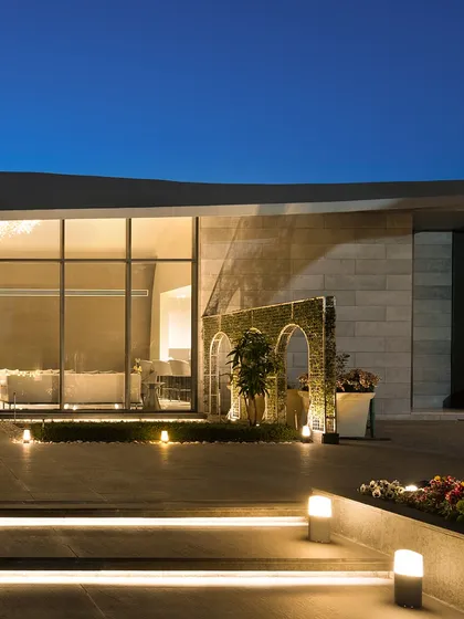 This perspective focuses on the entrance of the modern outhouse at dusk. The warm interior light spills out onto the patio, inviting guests in and showcasing the transparency and open nature of the design.