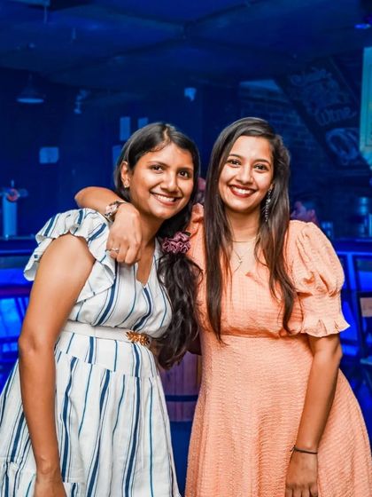 Two friends smiling for the camera in front of the well-lit bar.