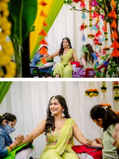 The bride is all smiles as her Mehendi is applied, surrounded by the vibrant colours of the ceremony's decor.