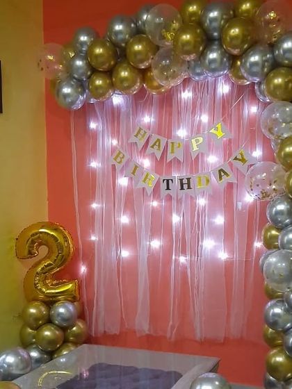 A 2nd birthday decoration in gold and silver, with a fairy light curtain backdrop.