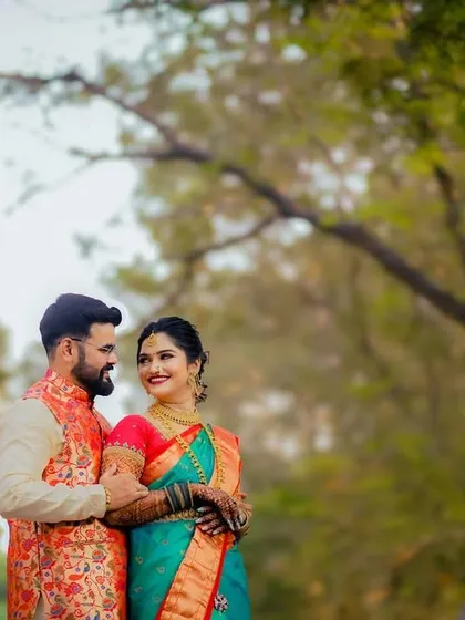 A classic portrait of a couple in colorful traditional outfits, sharing a happy moment under the trees.