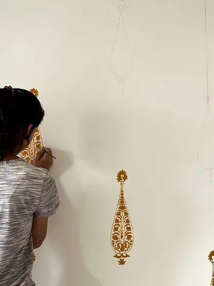 A member of my team carefully painting a traditional gold motif on a wall. This shows the collaborative nature of my studio's work.